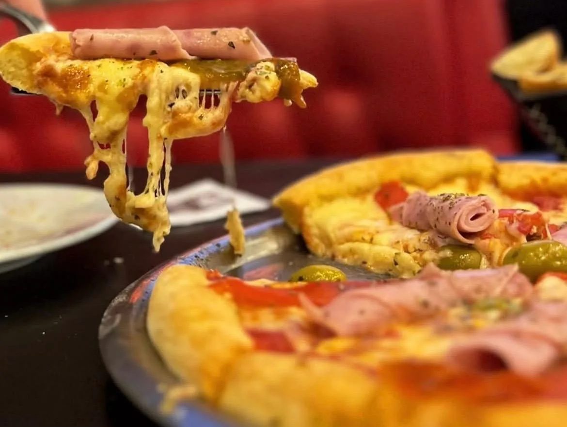 Porción de pizza con jamón levantándose con el queso fundido