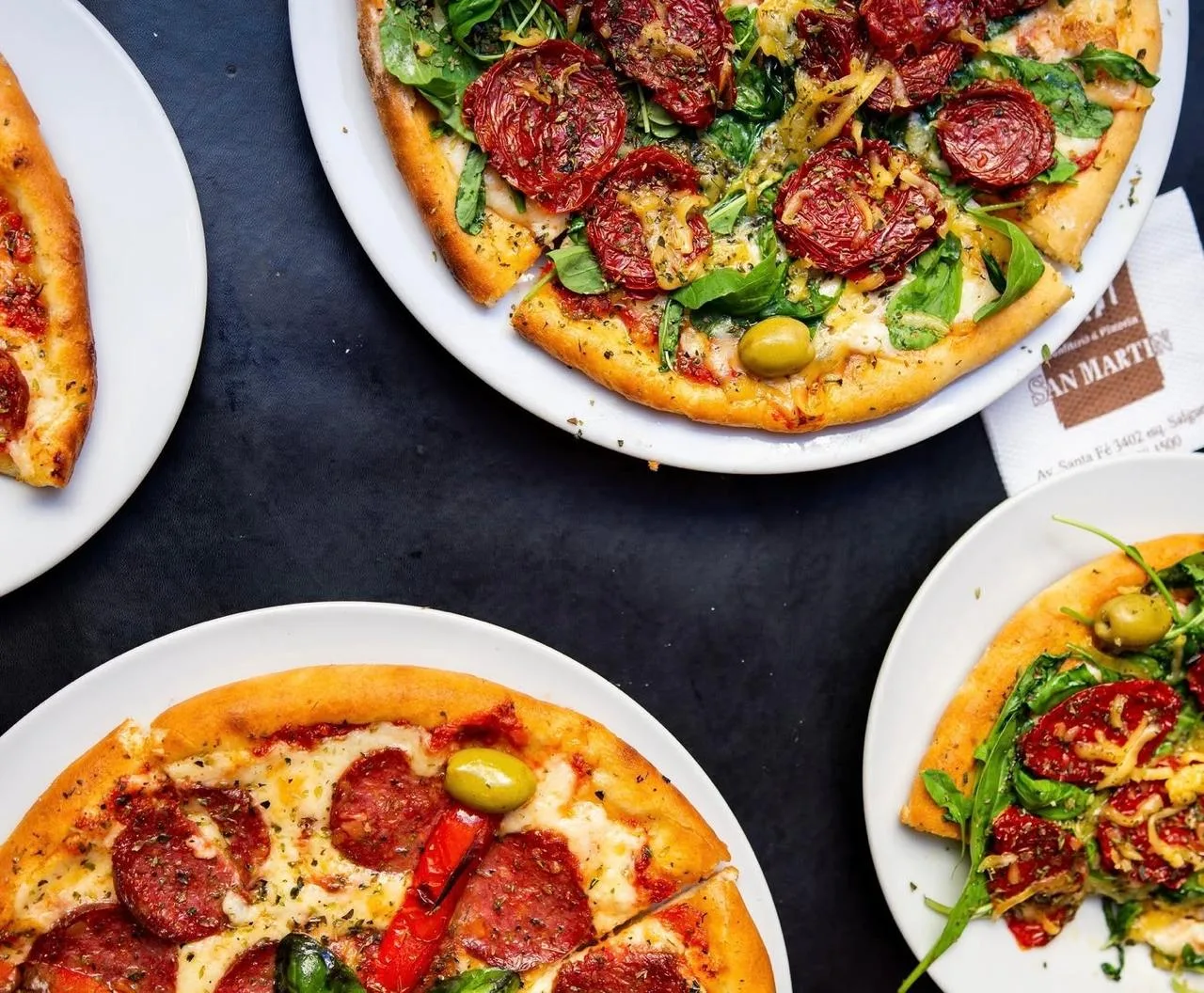 Cuatro pizzas al molde con distintos toppings servidas en la mesa